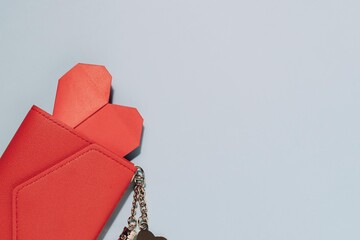 Red wallet with a hidden red heart and keychain on soft blue background. Perfect for themes of love, personal finance, and valuing heartfelt connections.