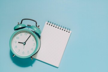 A teal twin bell alarm clock and blank notepad on blue. Perfect for themes of time management, planning, and starting schedules.