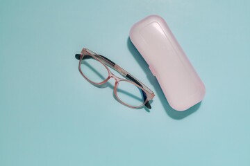 Pink framed glasses and matching case on soft blue background. Perfect for themes of eye care, vision accessories, and protecting personal items.