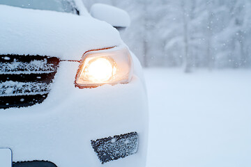 Car Headlight in Snow: A close-up of a car's front with a headlight illuminated, heavily covered in fresh snow, set against a snowy outdoor background.