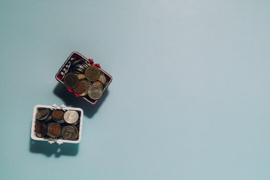 Mini red and white shopping baskets with coins on light blue background. Perfect for themes of saving, investing, and financial management.