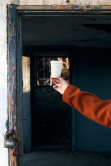 Hand holding coffee cup in abandoned building doorway with peeling paint and padlock