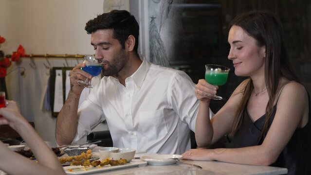 Couple or group friends making toast with cocktail gin tonic, blue hawaii, Cosmopolitan and Grasshopper at dinner table main course, lively conversation celebrating special party nightclub. Vinosity.