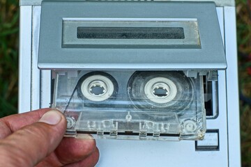 one plastic old stereo with a recording audio cassette with magnetic tape is inserted by hand into...