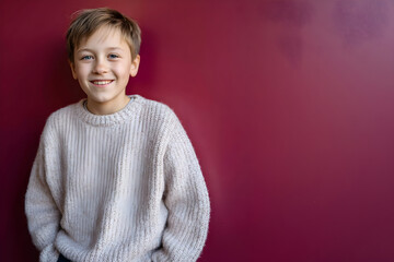 Young boy with cheerful expression stands casually against a colorful wall indoors