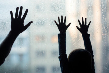 Silhouette of hands on rainy window glass, child and adult hands, rainy day feelings, indoor family time