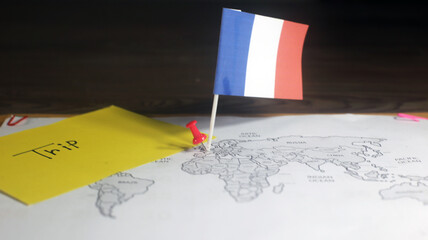 Travel to France concept, National Flag waving on world map with handwritten text trip in a yellow sticky note, on a wooden table