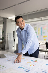 Chinese businessman, business professional or analyst stands next to desk covered with heap of...