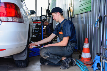Tire service technicians remove wheels from a car with wrenches inside the service center in their...