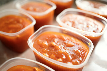 Plastic containers filled with homemade apricot preserve arranged on a light surface. Natural sweet...