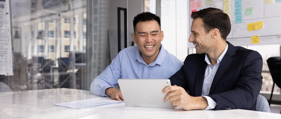 Happy teammates discussing project plan on tablet, laughing while reviewing project, read email or...