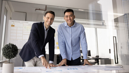 Portrait of two multiethnic project managers reviewing documentation, sales revenue or progress,...
