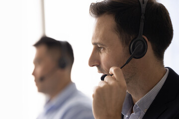 Close up of middle-aged man, call center employee wearing headset, leading talk with company...