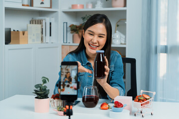 Smiling young beautiful Asian reviewing tasty mixed strawberry and cherry juice detox drinks,...