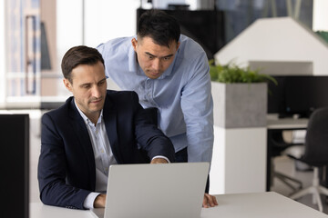 Two focused team members working together, checking tasks, timelines, or progress on project using...