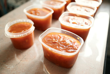 Homemade apricot preserve in multiple plastic containers placed on a marble surface in bright...
