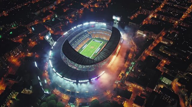 Aerial night view of illuminated football stadium in city center, surrounded by glowing urban lights, highlighting sports culture and event atmosphere