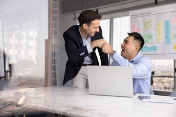 Positive diverse businessmen greeting each other, working together on project, engaged in effective, productive teamwork, getting happy, fist bumping, celebrate joint success, achieved corporate goal