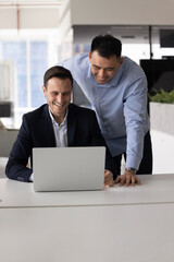 Two smiling multiracial men colleagues reviewing presentation or slideshow, researching...