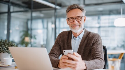 Smiling mature businessman holding smartphone sitting in office. Middle aged manager ceo using cell phone mobile apps and laptop. Digital technology applications and solutions for business developmen