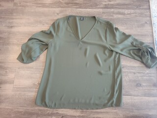 A beautiful green blouse with long sleeves is laying on a wooden floor
