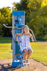 Young girl exercising on outdoor exercise machines. Woman exercising outdoors in the city park. Healthy lifestyle on city playground