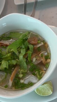 Vietnamese Chicken Soup warm bowl of Vietnamese chicken noodle soup with lime and fresh herbs being garnished adding red peper spicy