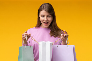 Close up shot of a young woman on yellow studio background holding shopping bags and looking inside...