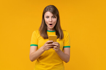 Young woman on yellow studio background reading a message on her smartphone with a surprised expression, capturing the moment of astonishment and curiosity from unexpected news or notification