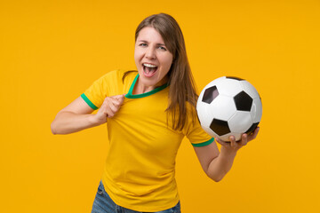 Young woman on yellow studio background holding a soccer ball and shouting with passion, expressing intense support as a fan or player, symbolizing the thrill of victory, betting, and competition