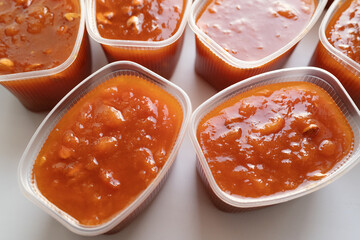 Close-up view of apricot preserve with fruit chunks in transparent plastic containers on a white...