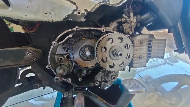 Detailed close-up of a motorcycle engine's internal components, including the clutch and gears, exposed during a repair or maintenance process. Focus on mechanical complexity.