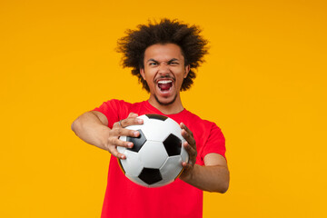 Young African American man poses on yellow background, passionately shouting while stretching a...