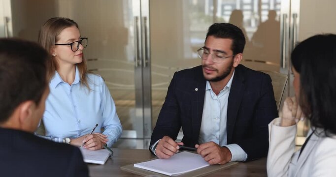 Serious confident young Middle Eastern businessman talking to coworkers, partners, stakeholders at office meeting table. Multiethnic business group discussing collaboration, market leadership