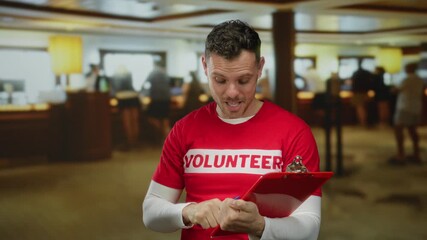 Young man in volunteer shirt holds clipboard inside hotel lobby confident expressive indoor male hospitality concept