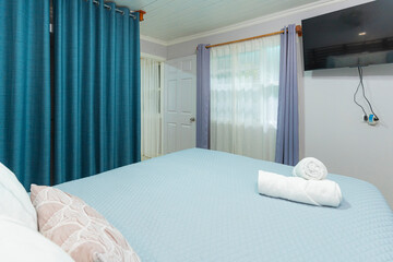 Bright bedroom with rolled white towels on bed and wall-mounted TV