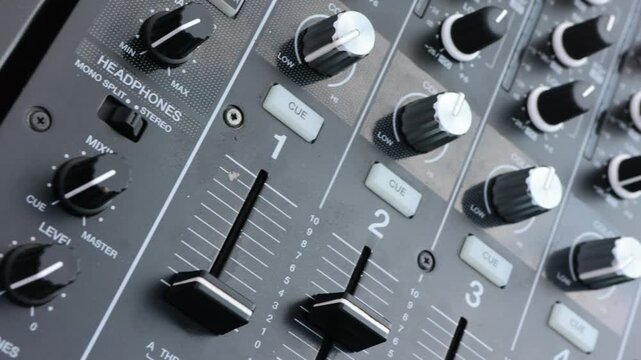 Close-up of a professional audio mixer's faders and knobs,