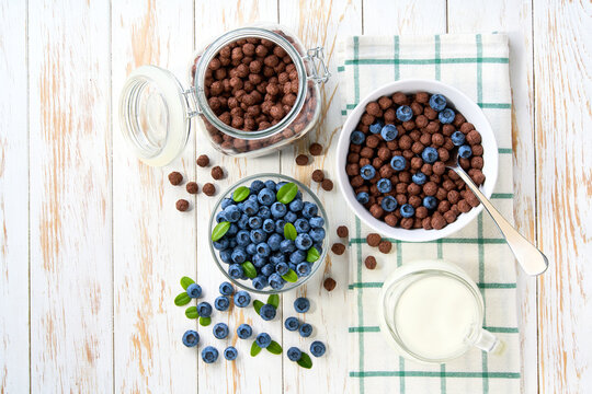 Healthy breakfast with chocolate corn balls and blueberry on a white wooden table, top view.