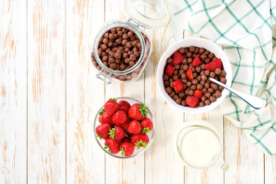Healthy breakfast with chocolate corn balls and strawberry on a white wooden table, top view.