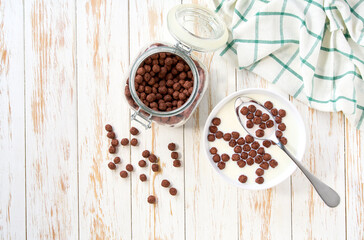 bowl of tasty chocolate corn balls with milk on a light kitchen table. Copy space for text. Top view.