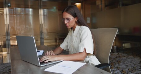 Serious Caucasian company CEO woman in elegant glasses working at computer at office workplace, typing on laptop, using online communication technology for business task solution