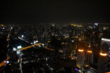 An ethereal nocturnal city panorama, adorned with twinkling lights from towering buildings and blurred highways, under a dark sky in Bangkok, Thailand. 