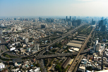 An aerial shot captures a sprawling urban landscape featuring towering buildings, complex highways, and bustling city life of Bangkok, Thailand. 