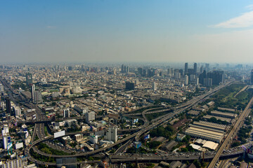 An aerial shot captures a sprawling urban landscape featuring towering buildings, complex highways, and bustling city life of Bangkok, Thailand. 