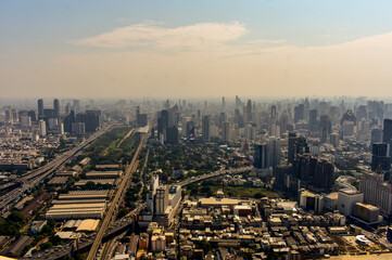 An aerial shot captures a sprawling urban landscape featuring towering buildings, complex highways, and bustling city life of Bangkok, Thailand. 