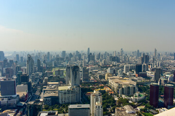 Panoramic urban skyline of Bangkok with numerous skyscrapers and buildings under a hazy sky.