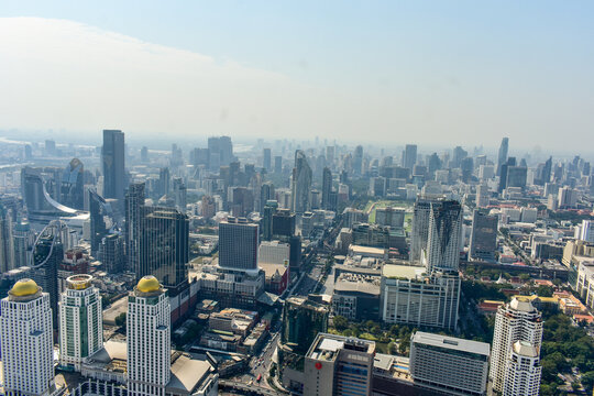 Panoramic urban skyline of Bangkok with numerous skyscrapers and buildings under a hazy sky.