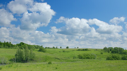 A scenic green landscape sprawls under a bright blue sky with fluffy clouds above