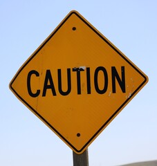 A caution traffic sign. The sign is diamond shaped, yellow in color with bold black letters. A thin...