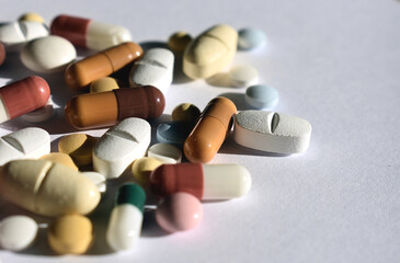 A macro shot of various medication pills and capsules in different colors on a clean white...